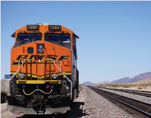 An orange train speeds through the desert on its tracks.